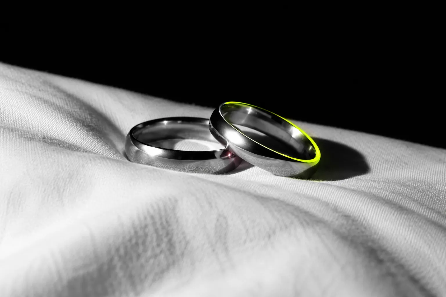 Two plain wedding rings on a white sheet, one edge lit yellow-green.
