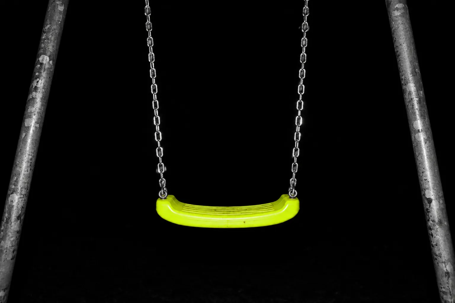 An empty playground swing at night, the seat bright yellow-green.